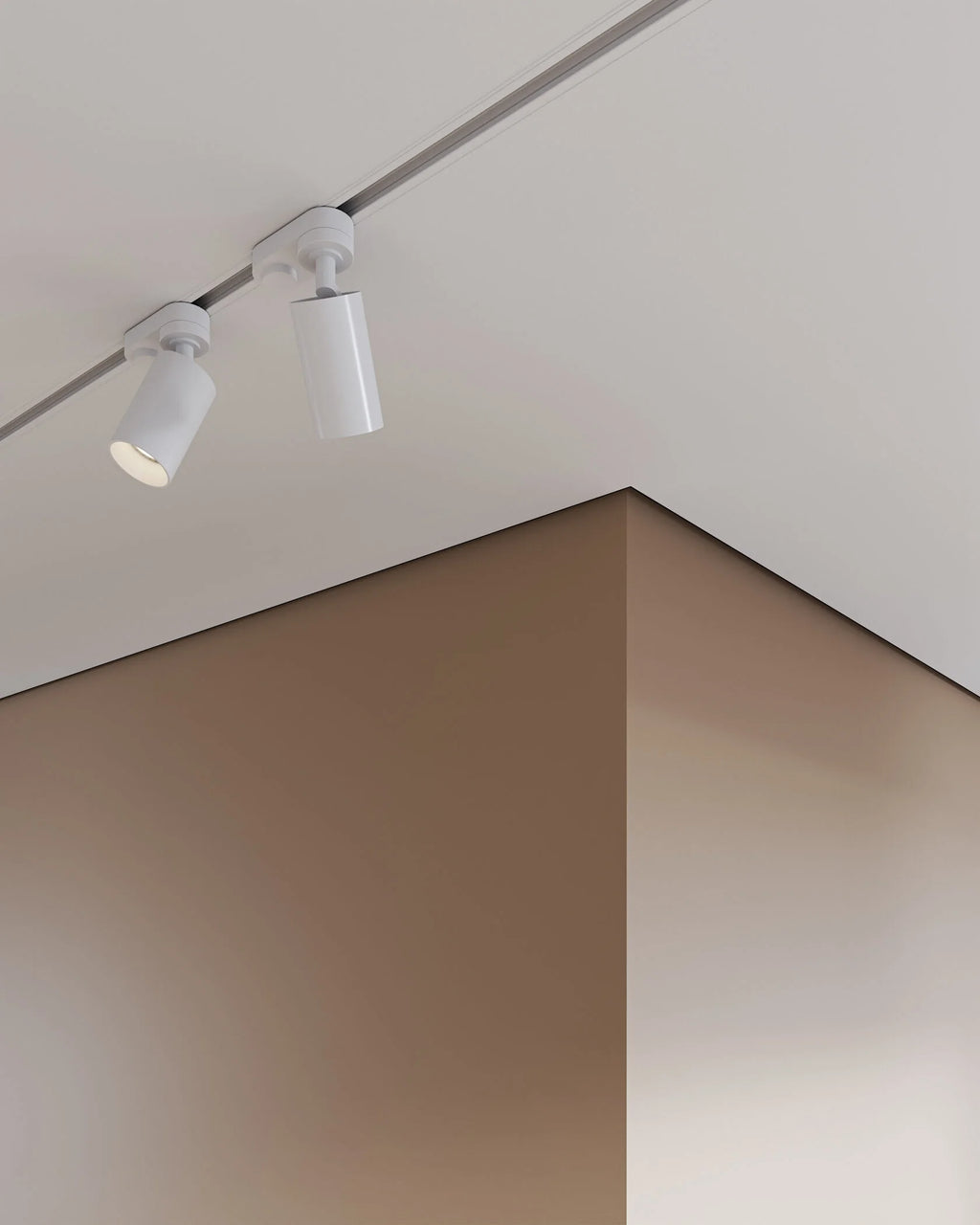 Two white cylindrical track spotlight fixtures mounted on a ceiling in a minimalist interior setting with warm beige and brown walls.