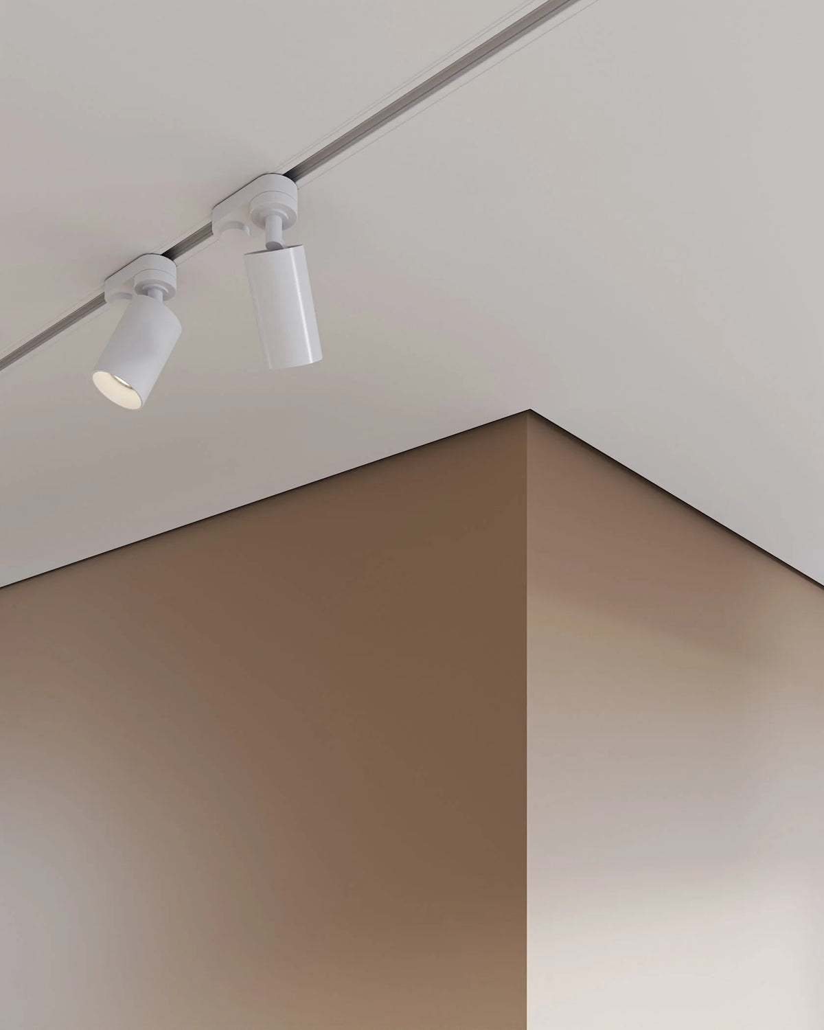 Two white cylindrical track spotlight fixtures mounted on a ceiling in a minimalist interior setting with warm beige and brown walls.