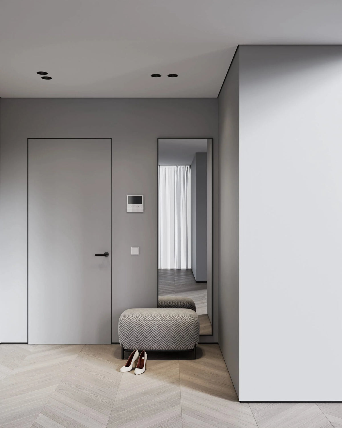 A modern minimalist interior hallway with a gray door, a tall floor mirror, a patterned gray ottoman, and light wood herringbone flooring.